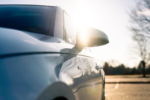 A car is parked in a parking lot. The sun is shining behind the car and the sunlight is reflecting off the car’s exterior.
