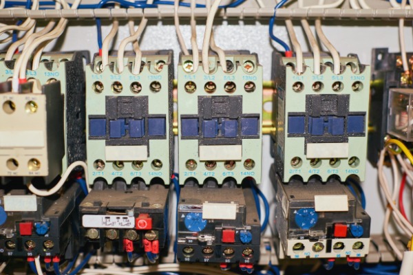A close-up of multiple old electrical relays and contactors in an electrical box filled with dirt and dust.